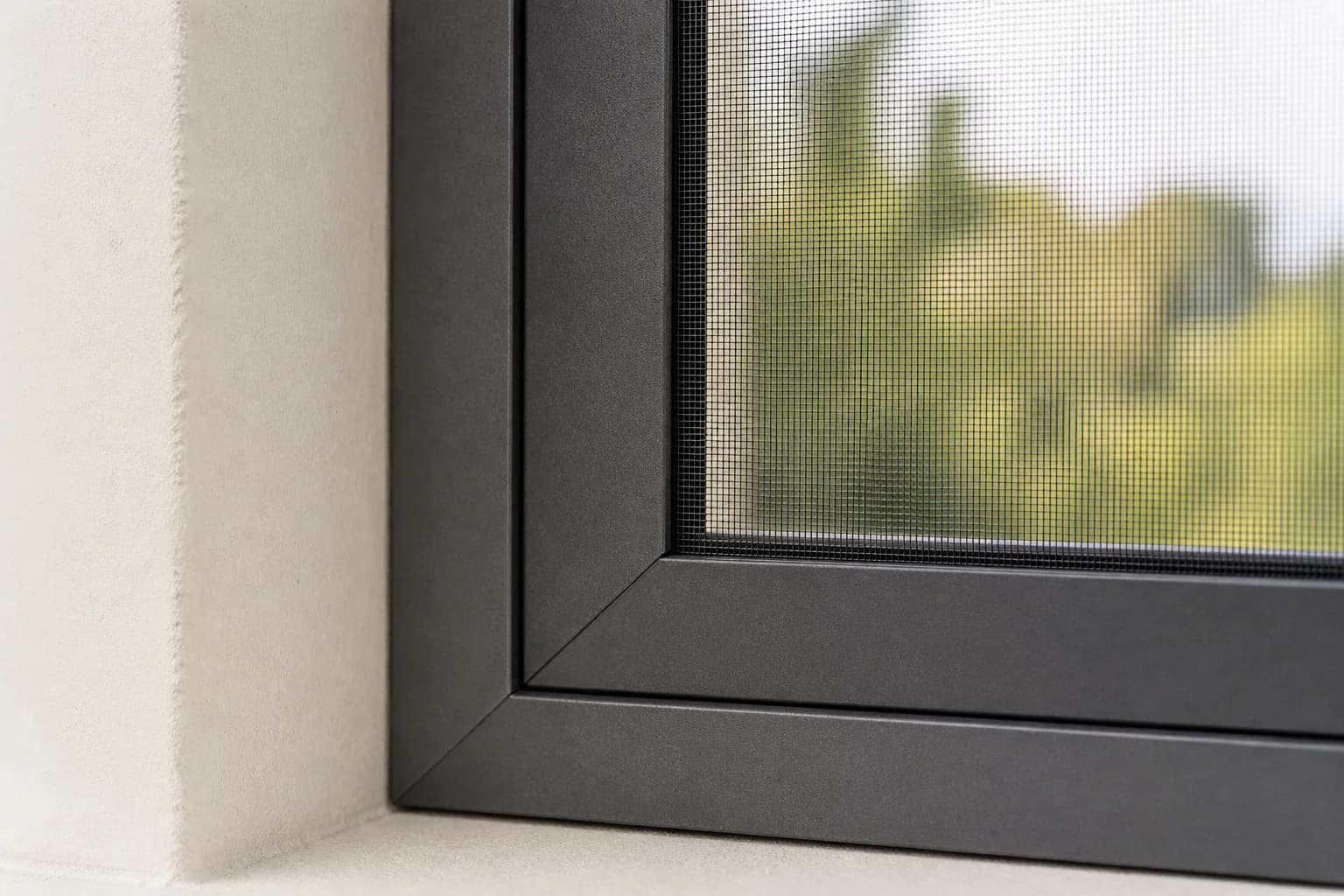 Ecke eines Insektenschutzrahmens in Anthrazit vor einem Fenster, dahinter unscharf Bäume